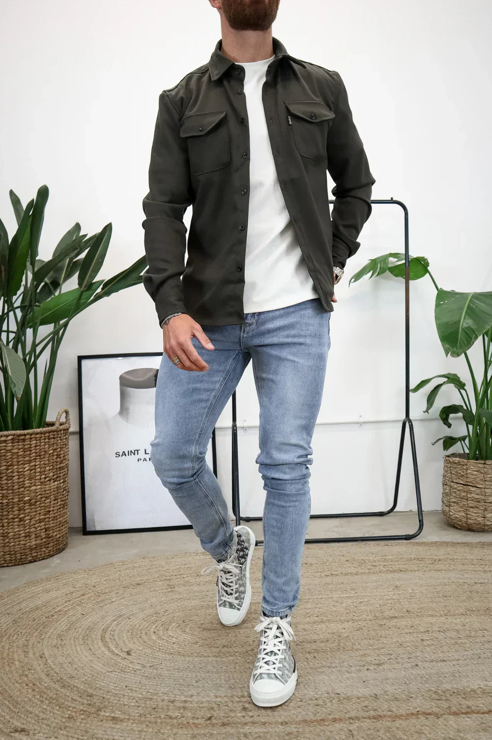 Dark green overshirt over white t-shirt and light jeans, standing indoors with decor.