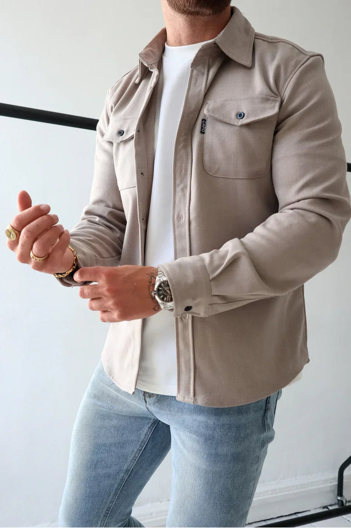 Taupe overshirt with buttons over white t-shirt and light jeans, person adjusting cuffs indoors.