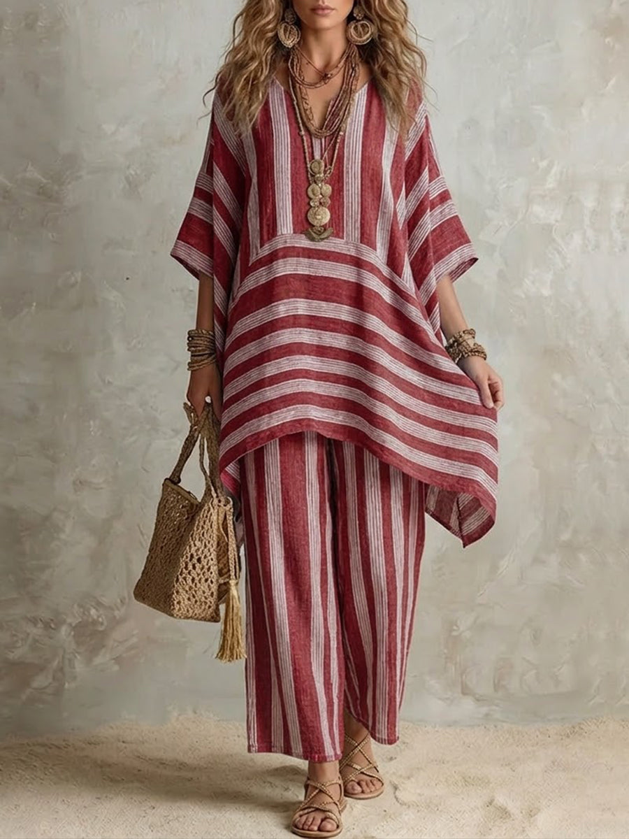 Red and white striped two-piece set with a draped top and wide pants, accessorized with layered necklaces and a woven bag, in a neutral studio setting.