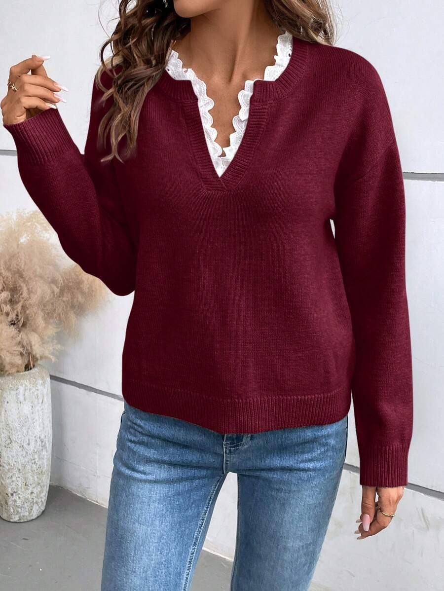 Red V-neck jumper with white lace detailing, styled with denim jeans. Indoor background featuring minimal decor.