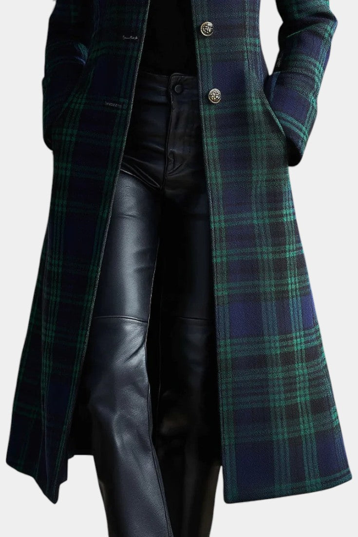 Close-up of a long plaid coat with ornate buttons, paired with black pants, shown in a studio setting.