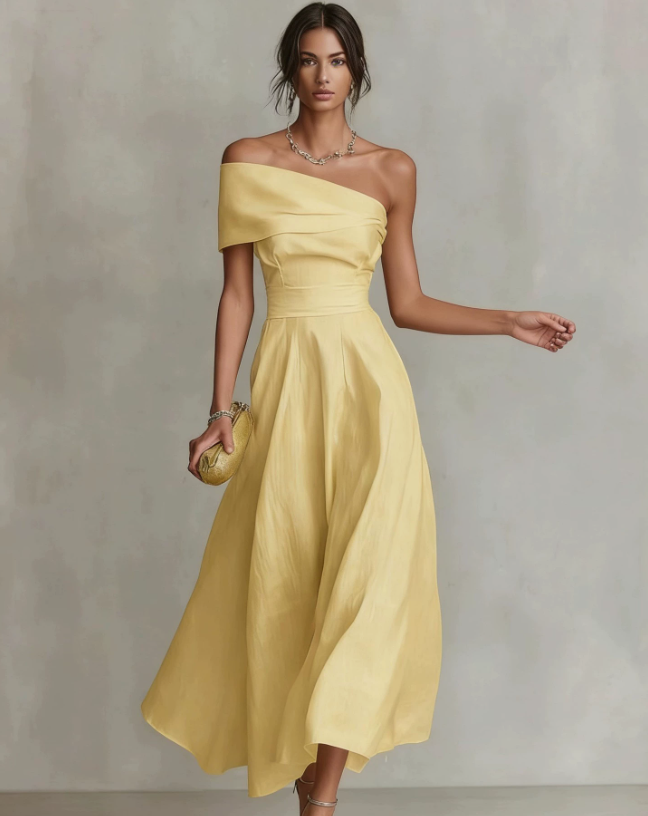 Elegant woman in a flowing yellow one-shoulder maxi dress, holding a clutch, in a neutral studio setting.