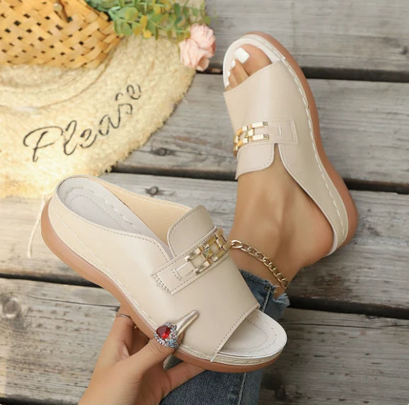 Beige elegant comfort sandals with gold accents on feet, displayed outdoors on wooden flooring with a decorative straw hat.