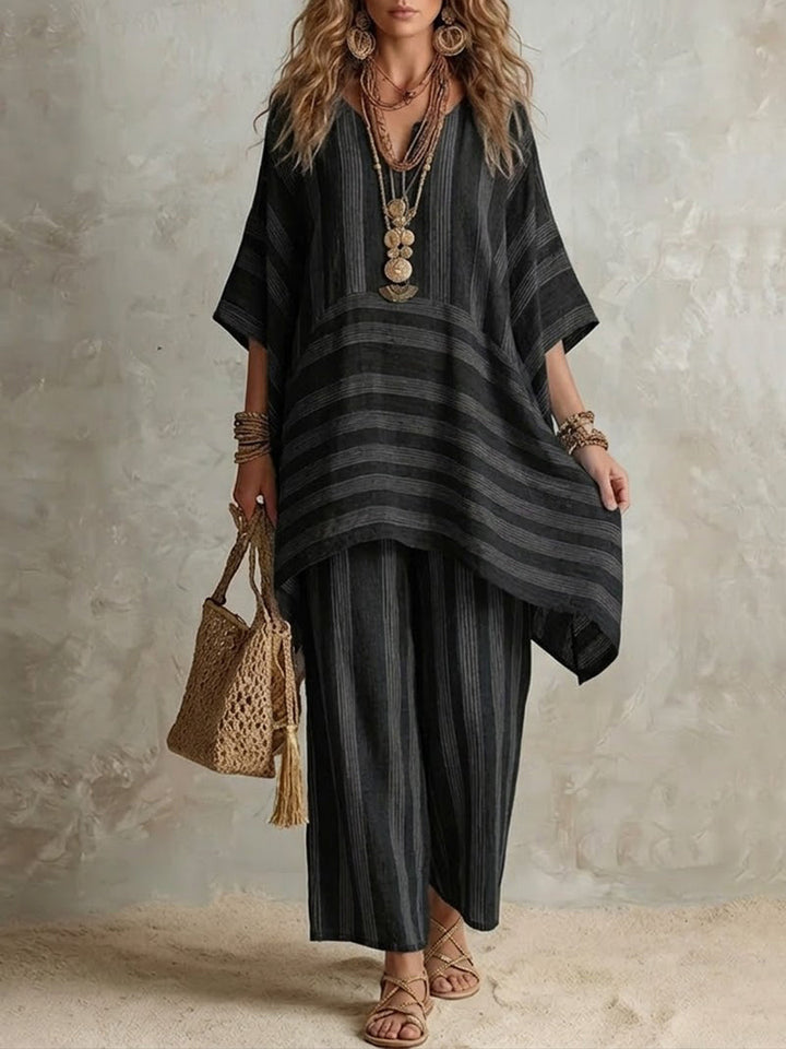 Black and dark gray striped two-piece set with a loose top and wide pants, styled with layered necklaces and a woven bag, in a neutral studio setting.