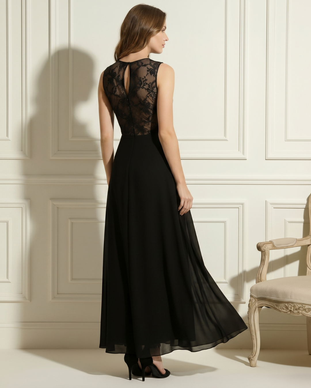 Back view of black dress highlighting lace detail and flowing fabric, in an elegant studio with ornate paneling.