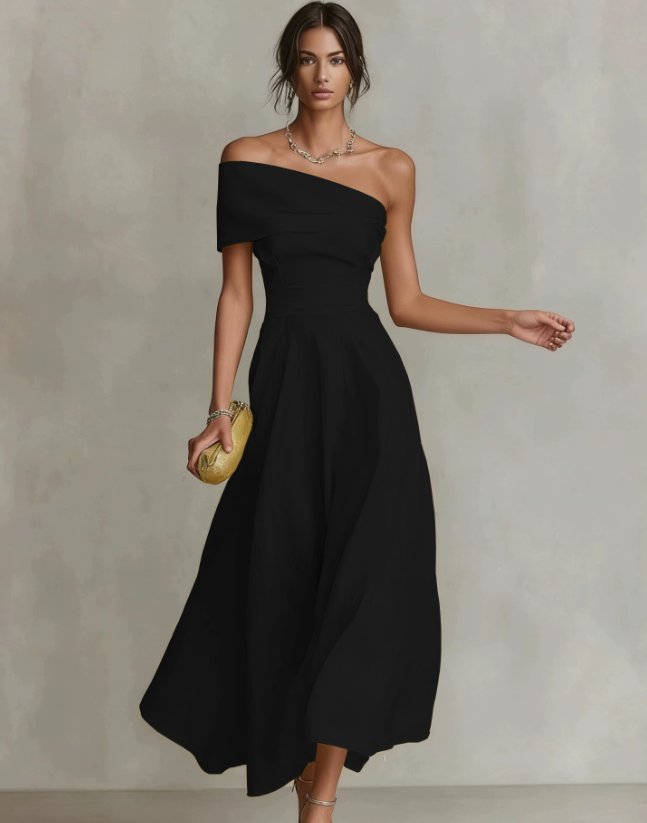 Elegant woman in a flowing black one-shoulder maxi dress, holding a clutch, in a neutral studio setting.