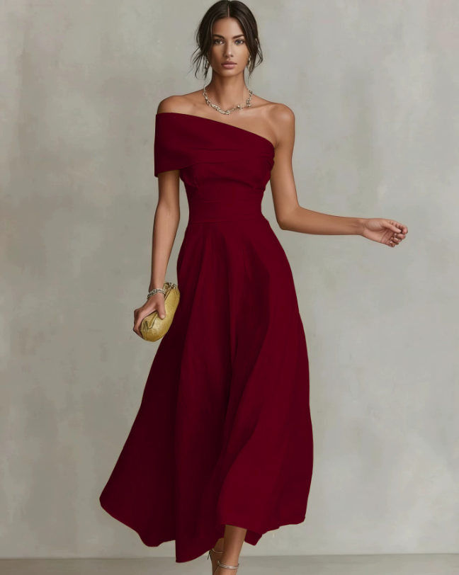 Elegant woman in a flowing burgundy one-shoulder maxi dress, holding a clutch, in a neutral studio setting.