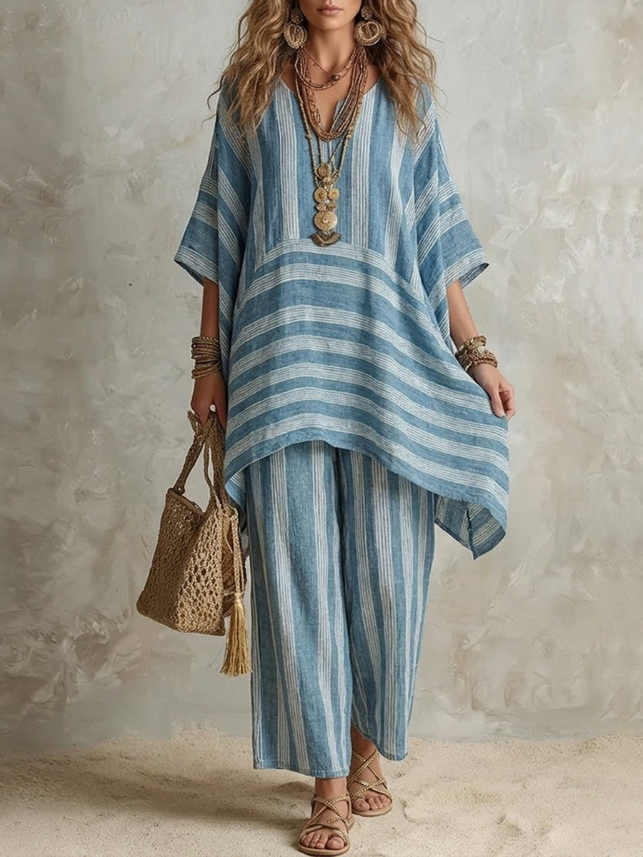 Blue and white striped two-piece set featuring a loose top and wide pants, complemented by layered necklaces and a woven bag, in a neutral studio setting.