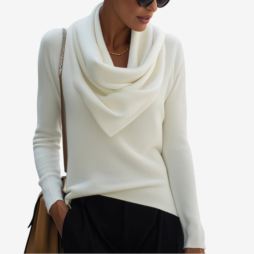 White draped neck sweater with long sleeves, paired with black pants in a minimalist studio setting.