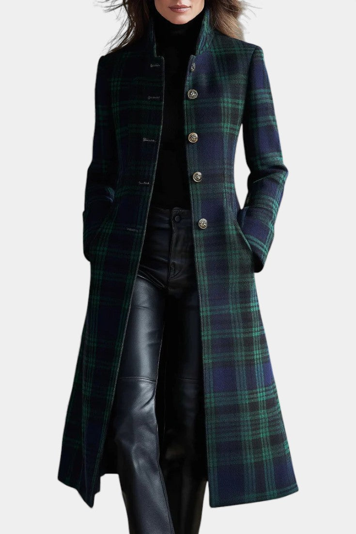 Front view of a long plaid coat in dark green and navy, featuring ornate buttons, worn over a turtleneck and pants in a studio setting.