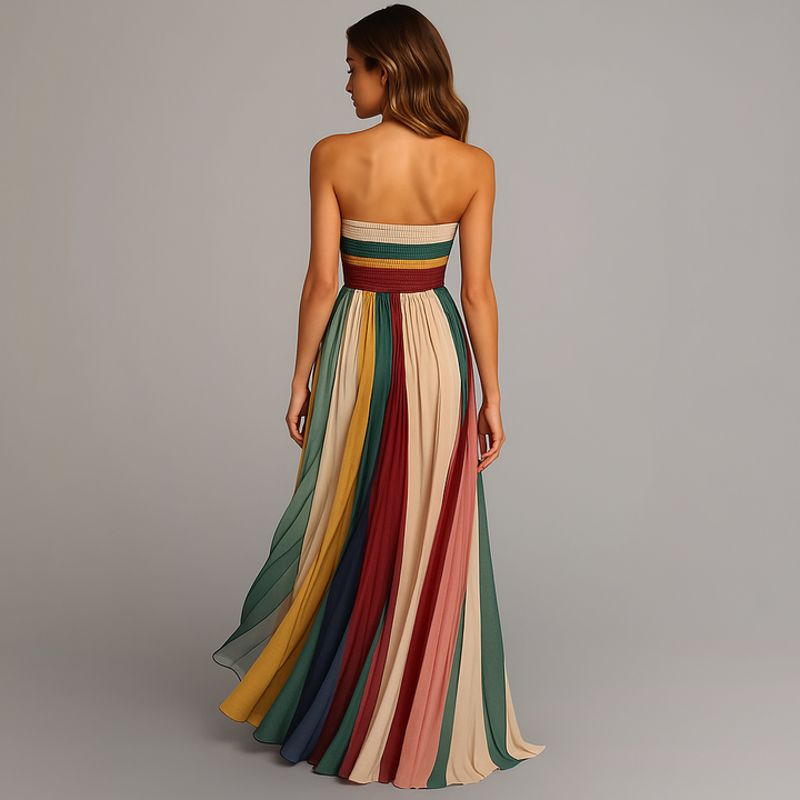 Rear view of a woman in a strapless colorful pleated maxi dress against a studio backdrop.