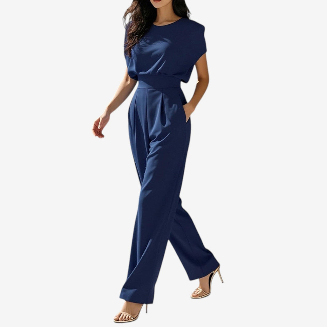 Navy blue sleeveless jumpsuit with wide legs, worn by model walking in studio setting with heels.