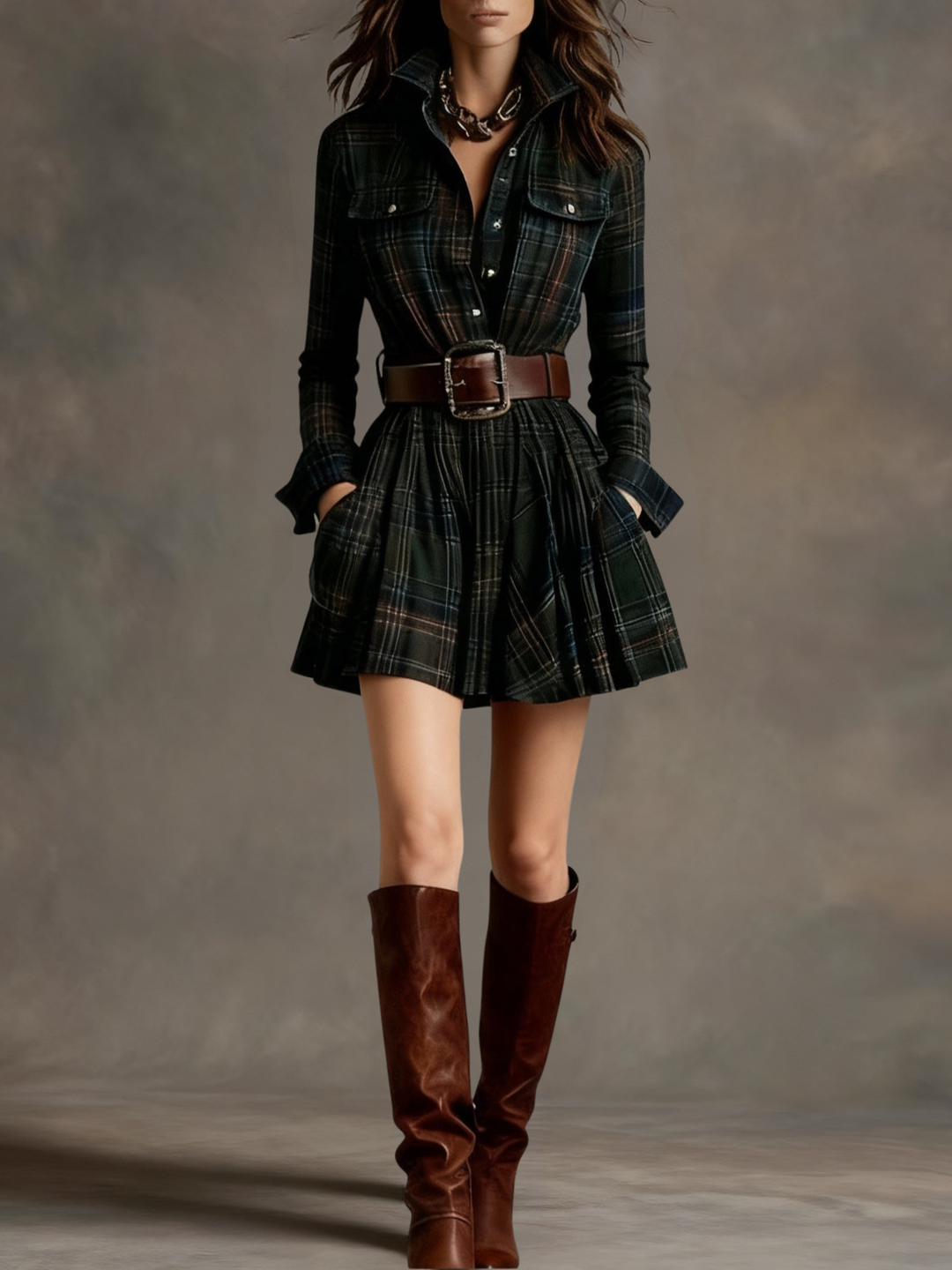 Plaid mini dress with structured belt and knee-high boots on a model in a studio background.