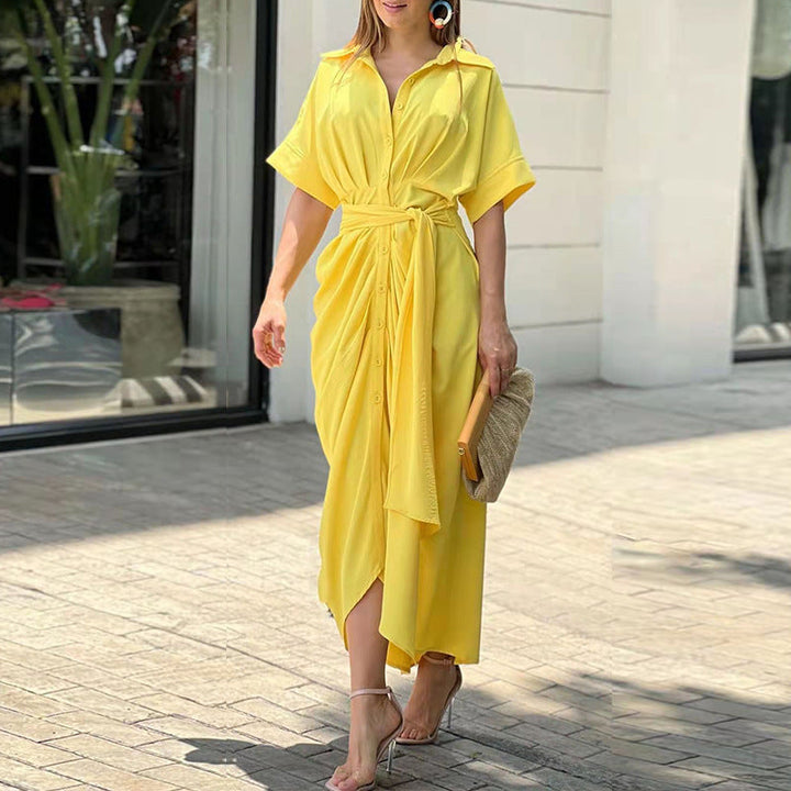 Yellow wrap maxi dress with structured waist, worn outdoors in a sunny setting by a glass storefront.