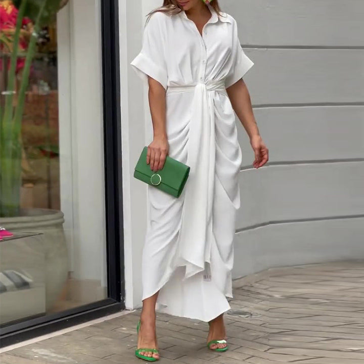 White wrap maxi dress with gathered waist, worn outdoors with a green clutch and vibrant shoes near a storefront.