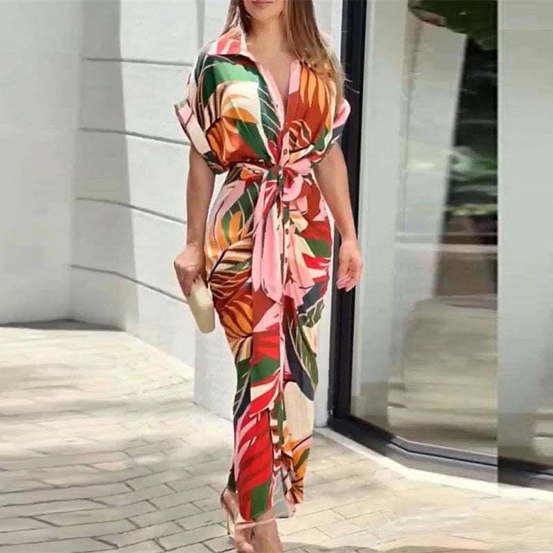 Colorful floral wrap maxi dress featuring pink, green, and orange hues, worn outside a contemporary building.