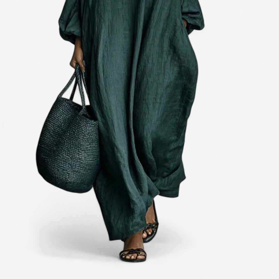 Flowing emerald dress with a woven bag and black sandals, studio background.