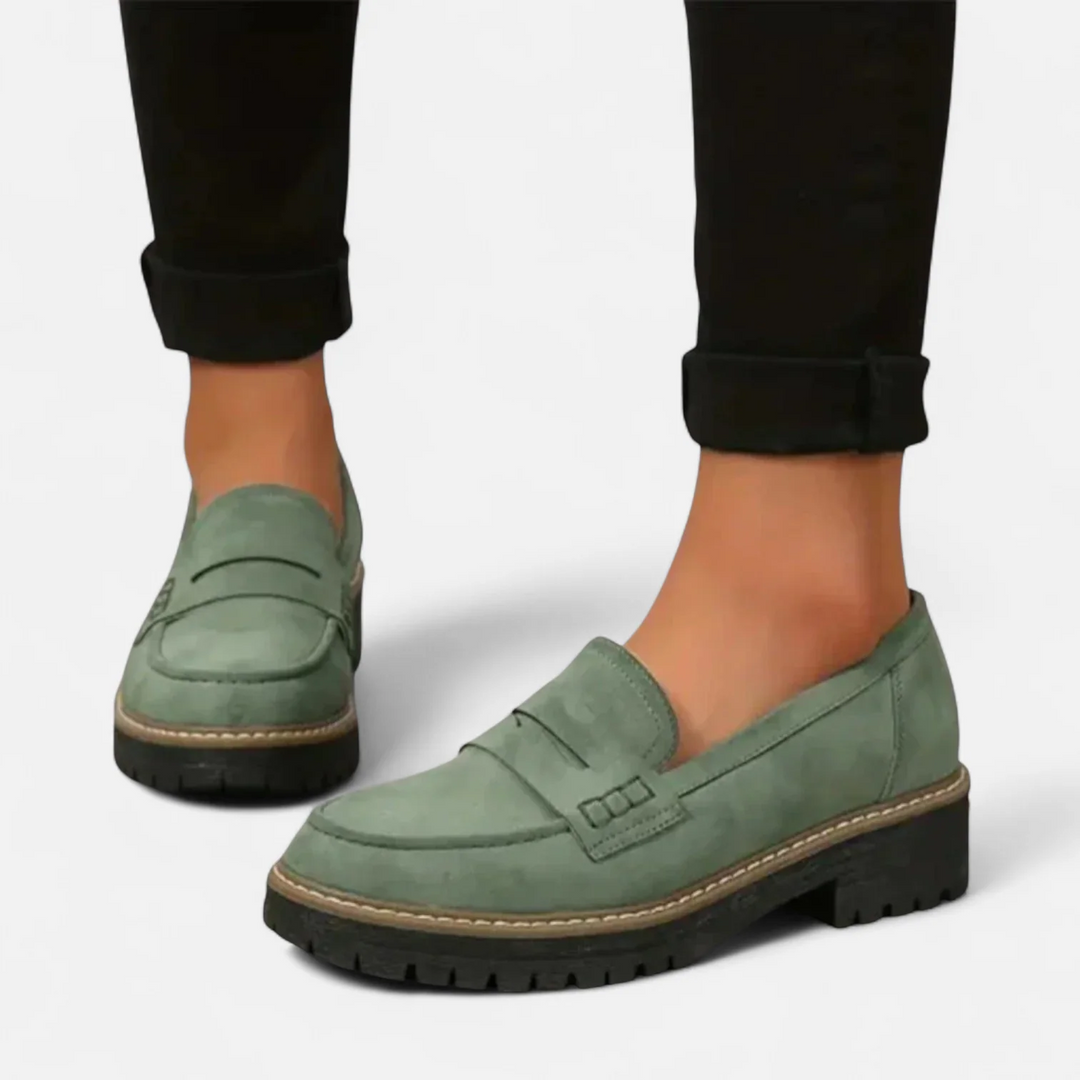 Green orthopedic moccasins worn with black cuffed pants, on a white background.