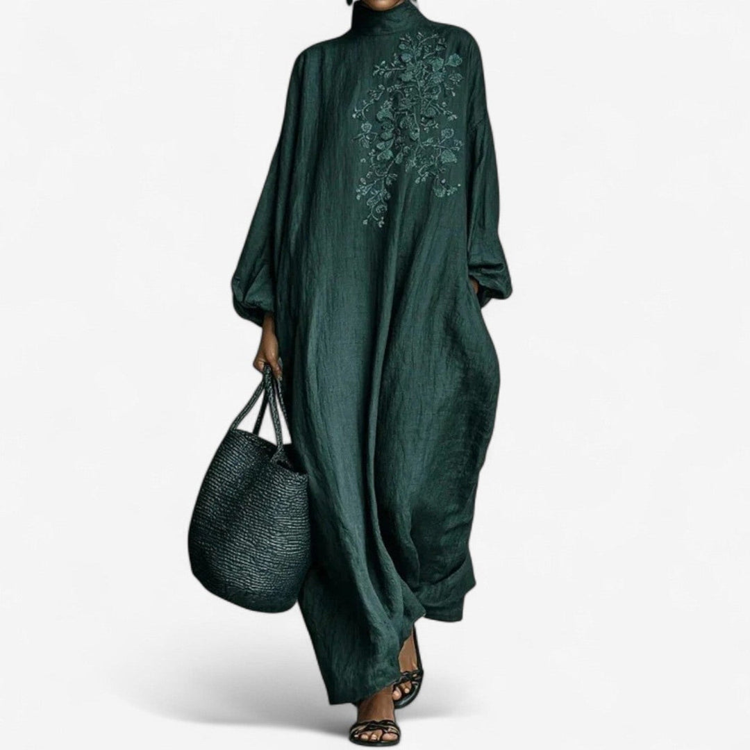 Elegant long emerald dress with floral embroidery, paired with a woven bag and sandals, studio background.