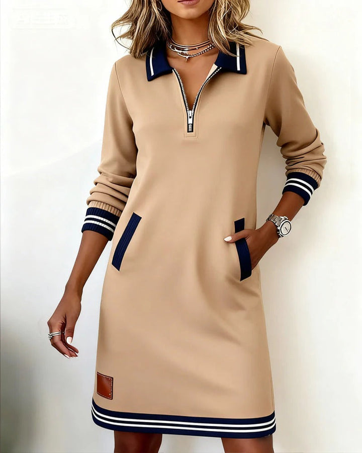 Light brown zip-front dress with navy details and practical pockets, showcased in a bright, minimal space.
