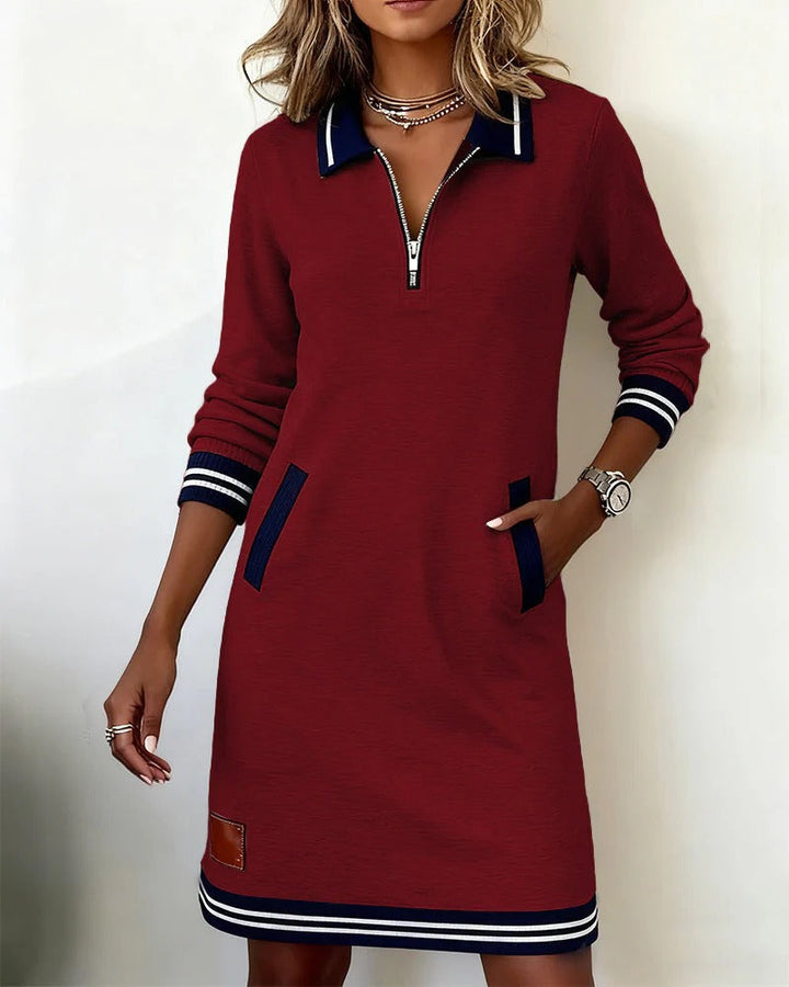 Crimson zip-front dress with navy details and side pockets, displayed in a bright, minimalist setting.