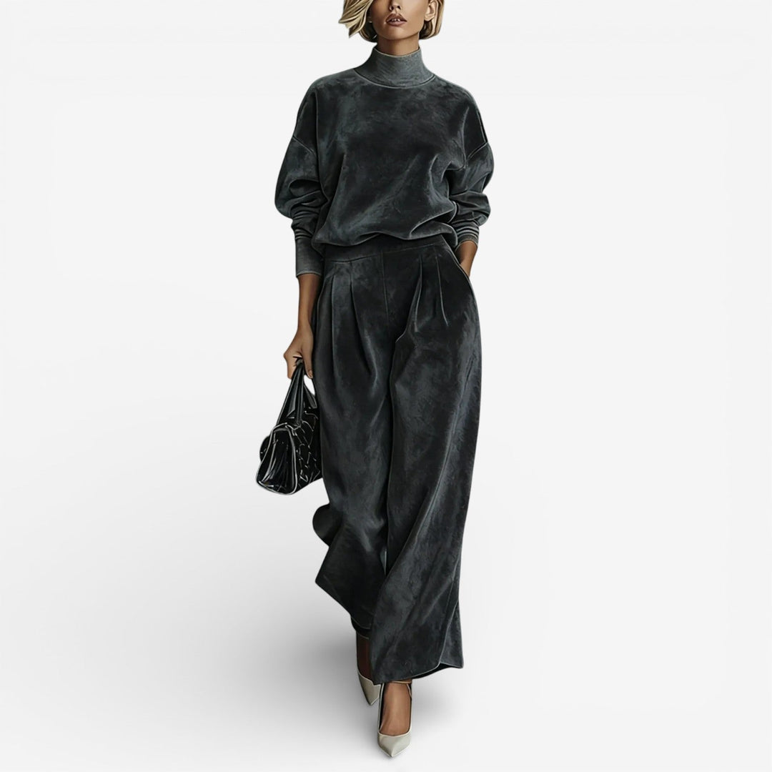 Model wearing charcoal contemporary set with a turtleneck and wide-leg pants, holding a black bag, on white background.