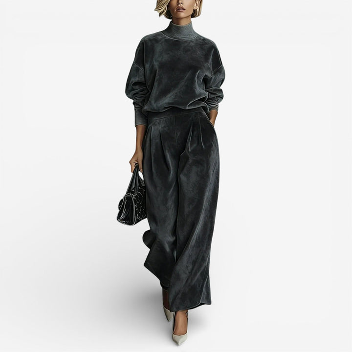 Model wearing charcoal contemporary set with a turtleneck and wide-leg pants, holding a black bag, on white background.
