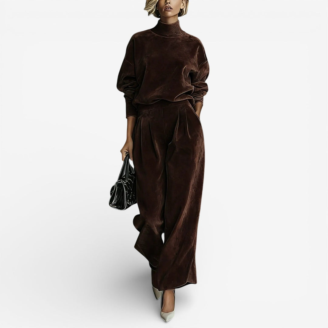 Model in chocolate brown contemporary set with turtleneck and wide-leg pants, carrying a black bag, on a light background.
