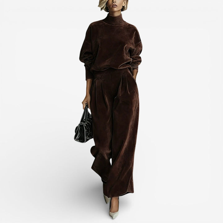 Model in chocolate brown contemporary set with turtleneck and wide-leg pants, carrying a black bag, on a light background.