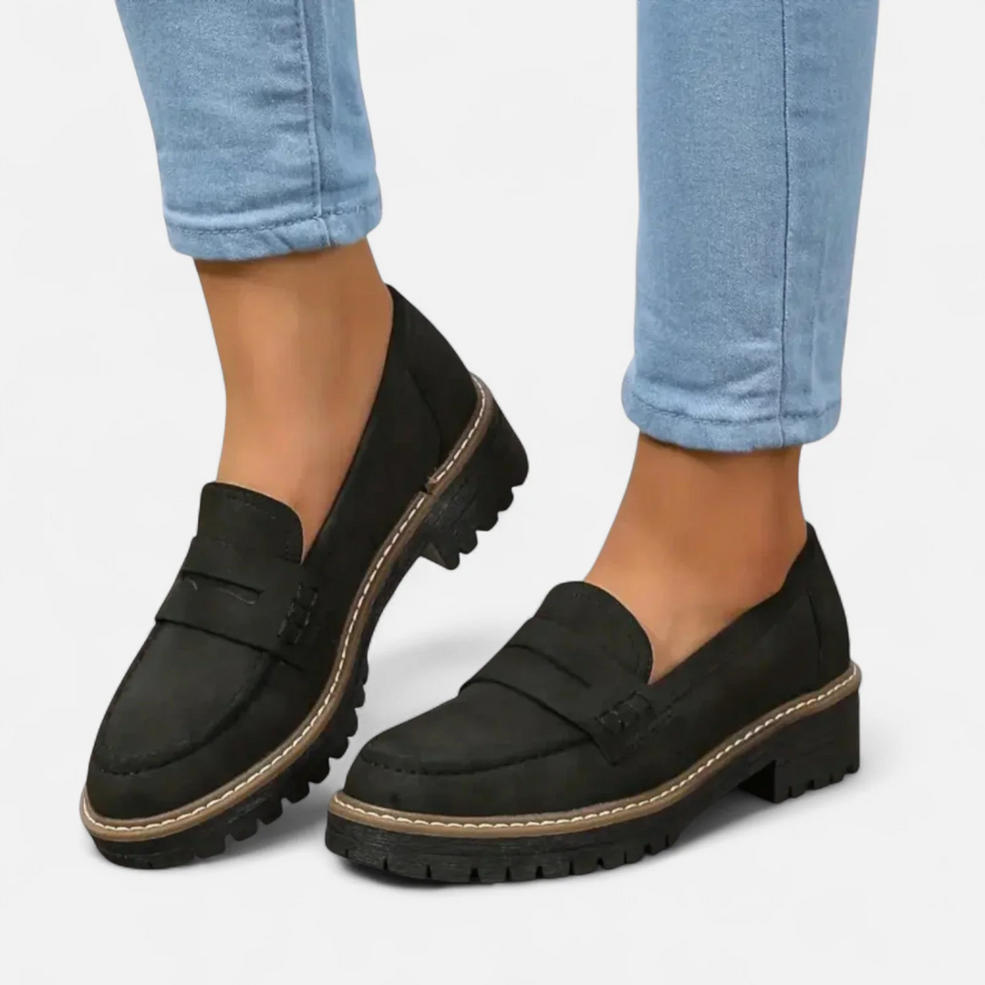 Black loafers with textured sole, worn with light blue jeans on a white background.