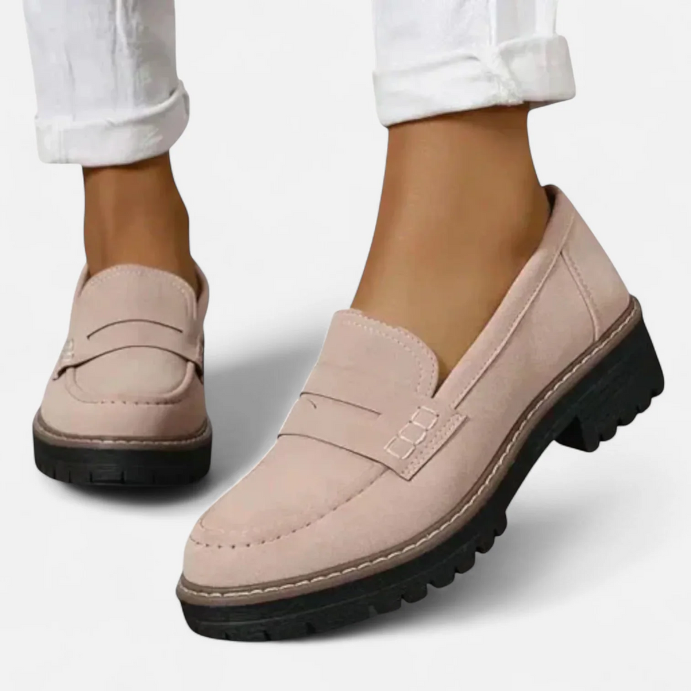 Light pink loafers with dark sole, worn with white rolled-up pants against a plain white backdrop.