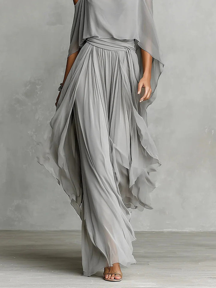 Gray flowy skirt with off-shoulder top modeled in a studio against a gray textured backdrop.