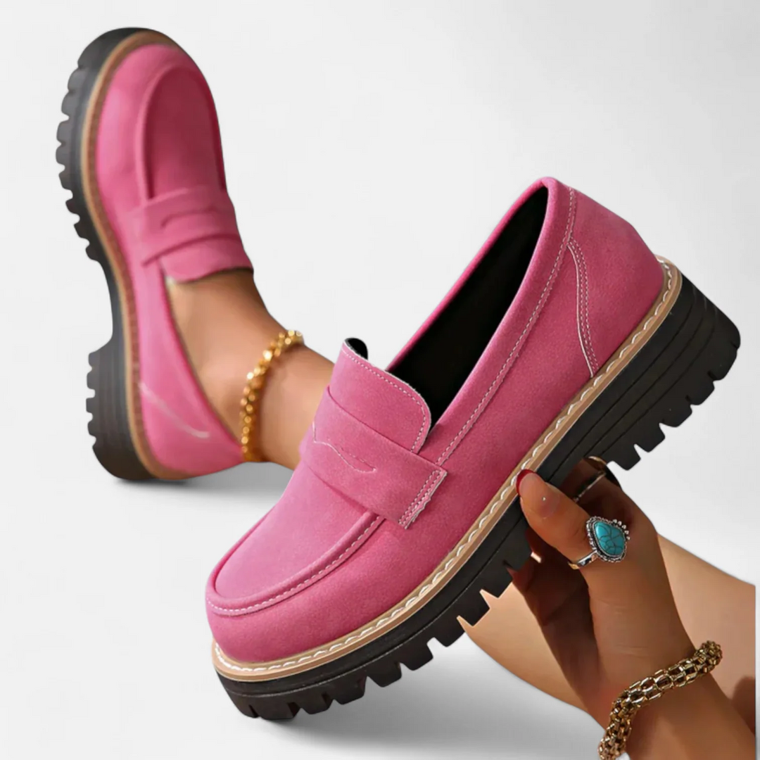 Vibrant pink orthopedic moccasins held in hand, accessorized with bracelets, on a white background.
