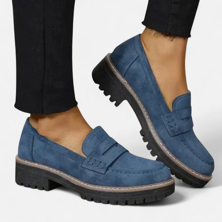 Blue orthopedic moccasins worn with black pants, set against a white background.