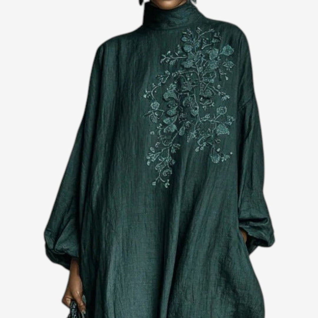 Close-up of emerald dress with intricate floral embroidery on chest, studio background.