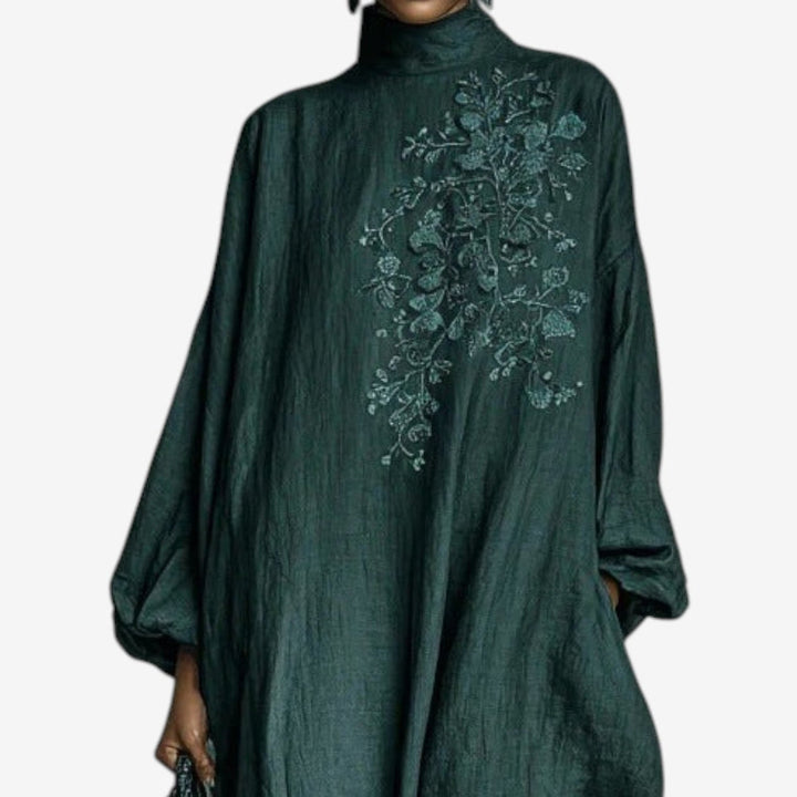 Close-up of emerald dress with intricate floral embroidery on chest, studio background.