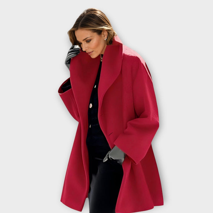 Woman modeling a vibrant red hooded coat with wide lapels in a studio.