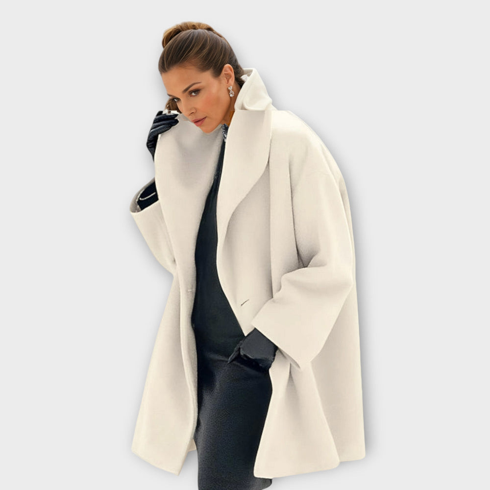 Woman in a white hooded coat with wide lapels indoors against a plain backdrop.