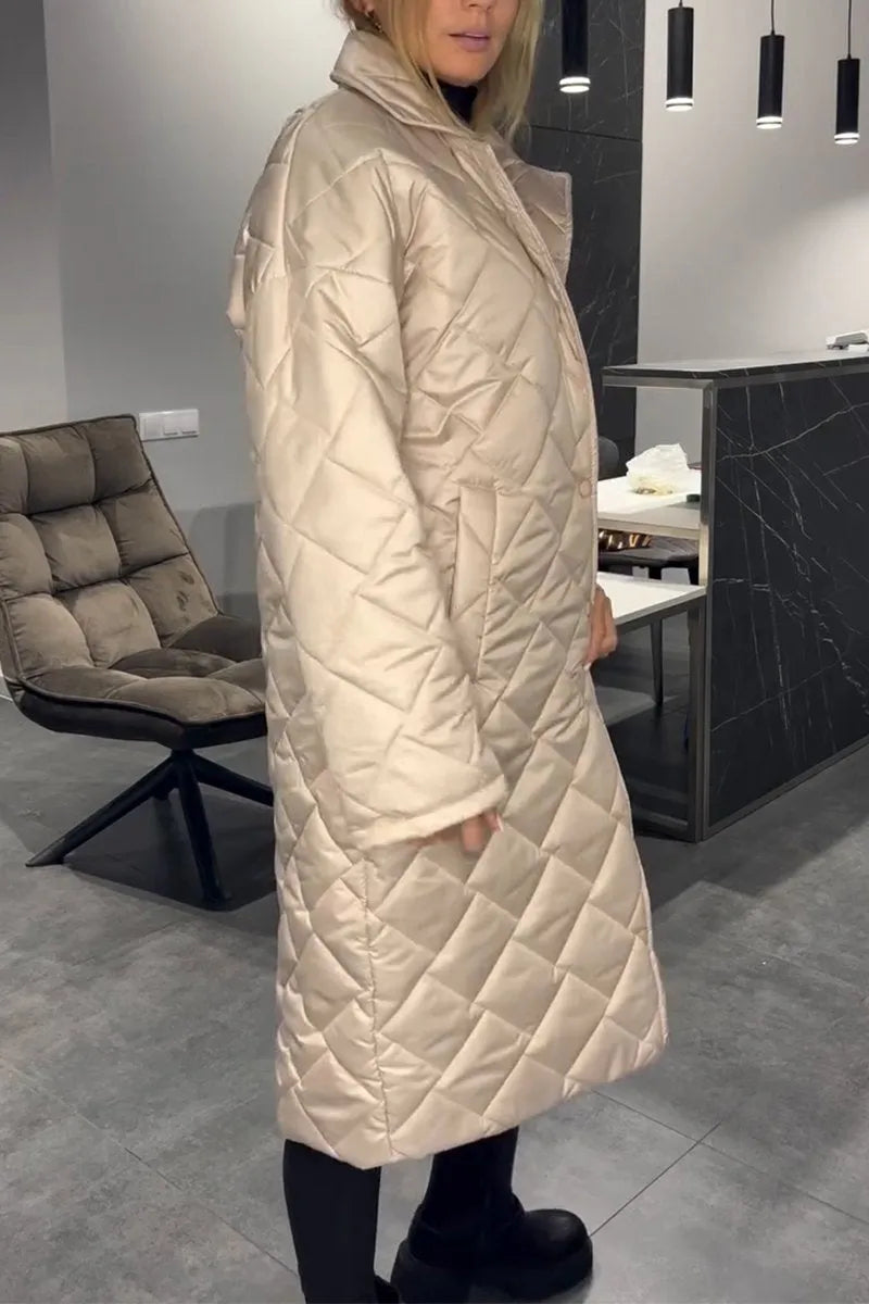 Side view of model wearing a light beige quilted coat, in a modern setting with gray flooring and a cushioned chair.