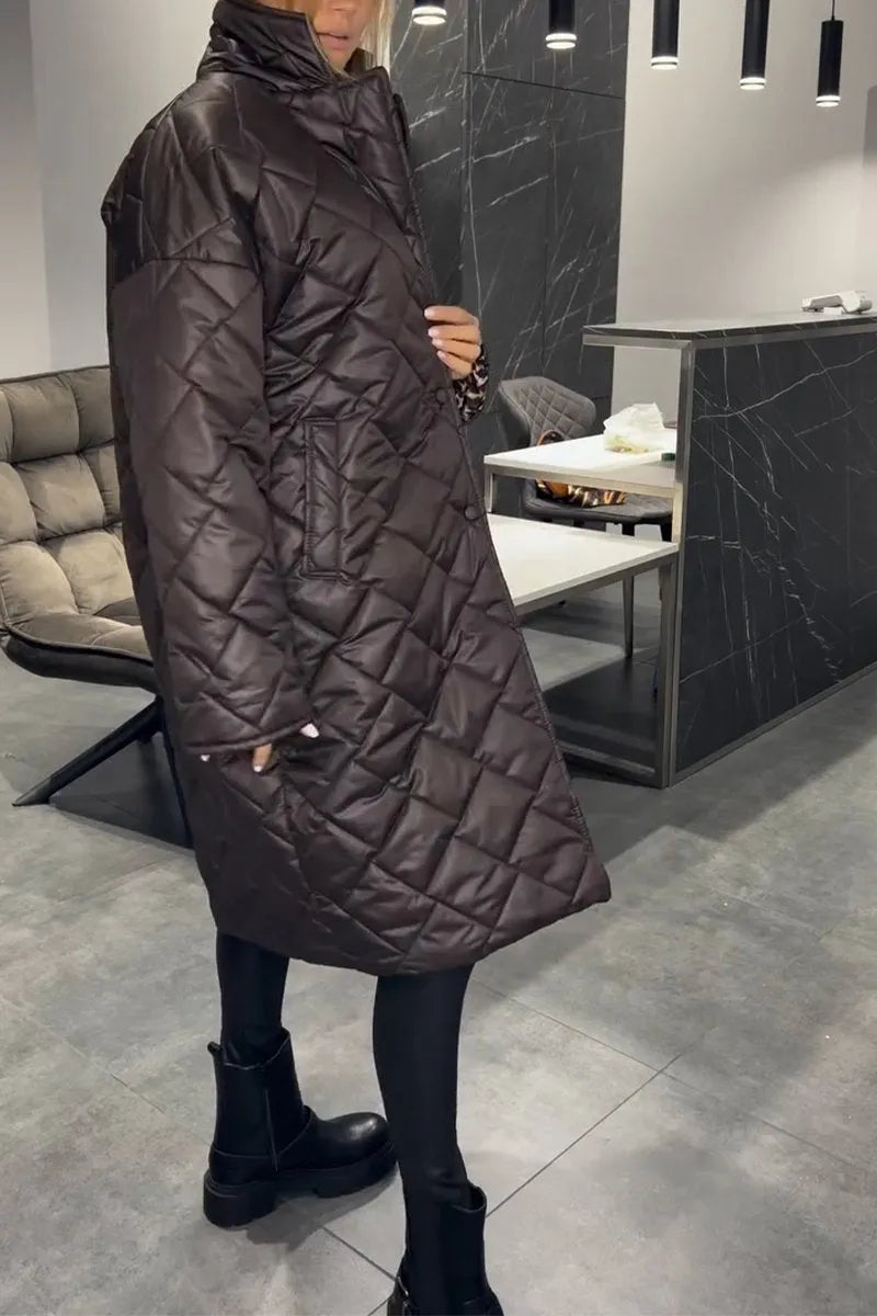 Side view of a model in a dark brown quilted coat, in a modern indoor setting with gray floors and a cushioned chair.