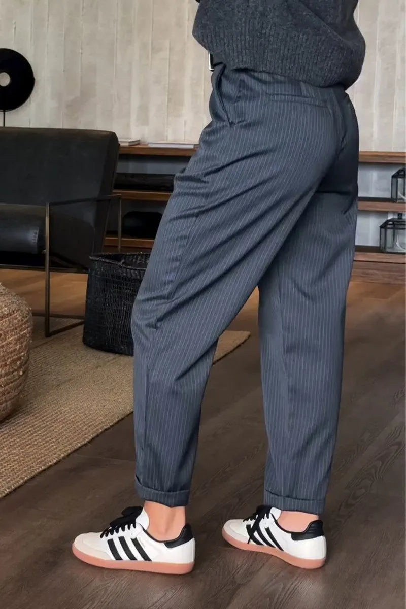 Gray pinstripe tailored pants featured in an indoor setup, complemented with a black belt and casual sneakers.