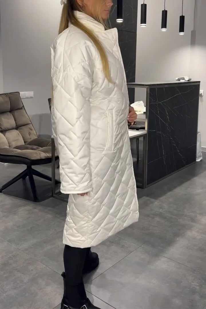 Side view of model in a white quilted coat, in a modern indoor space with gray flooring and modern furnishings.