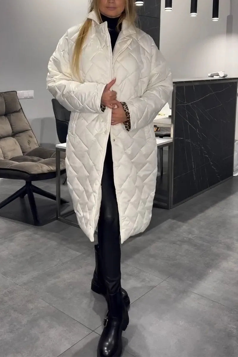 Model in a white quilted coat, standing indoors with tiled flooring and a cushioned chair in the background.