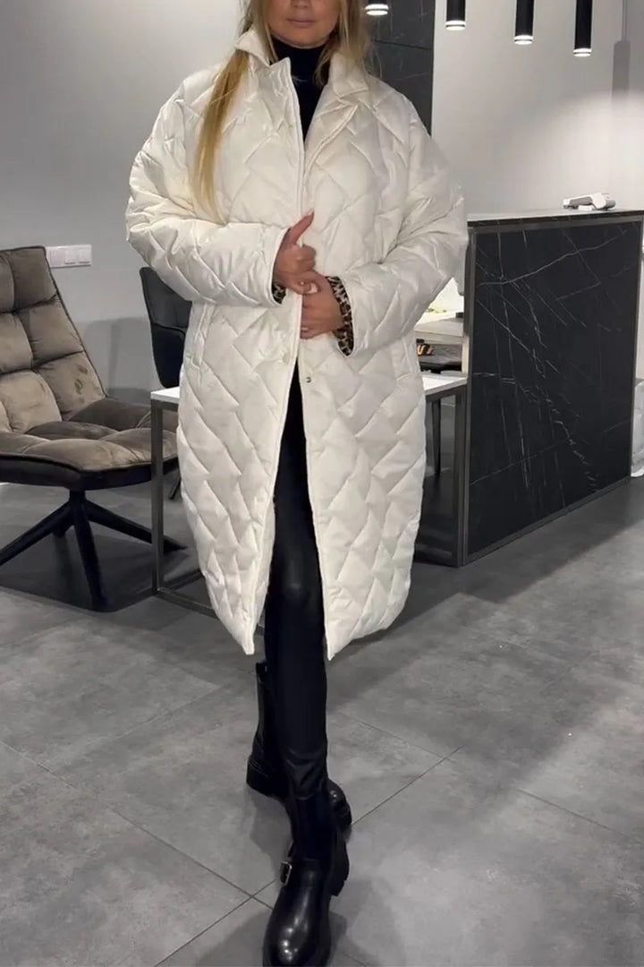 Model in a white quilted coat, standing indoors with tiled flooring and a cushioned chair in the background.