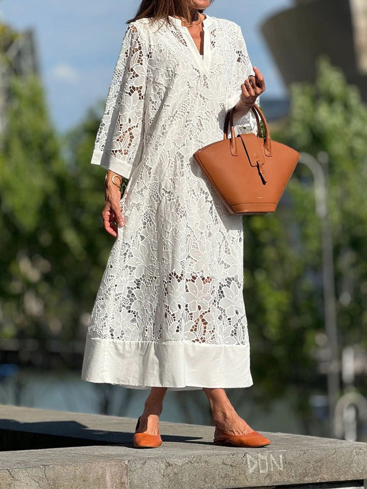 Elegant white dress with intricate cutout design worn by person with brown handbag and shoes, standing outdoors.