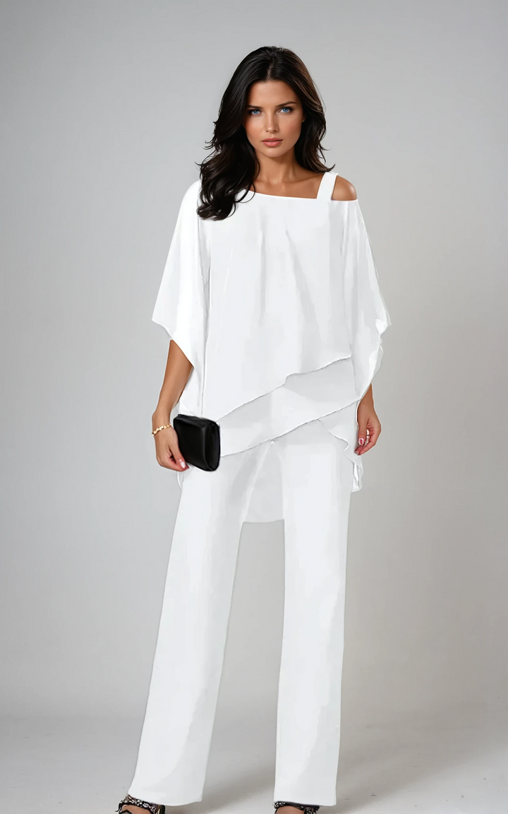 Woman in white two-piece layered set holding a black clutch in a studio setting.