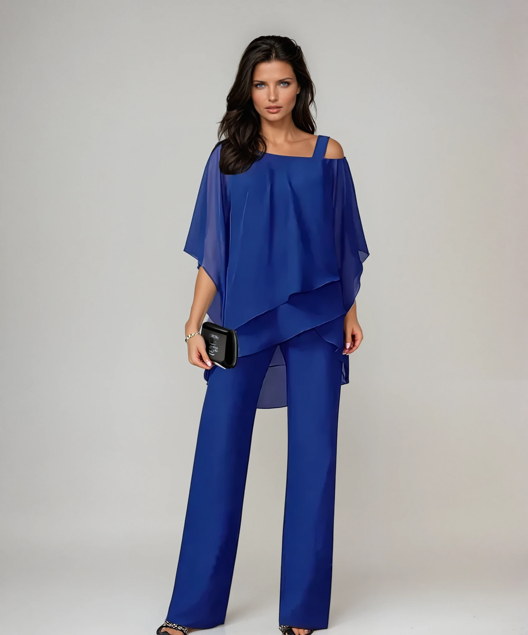 Person in a blue two-piece layered set carrying a black clutch in a studio environment.