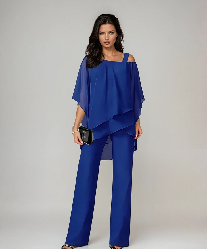 Person in a blue two-piece layered set carrying a black clutch in a studio environment.