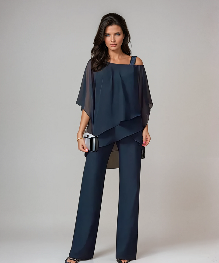 Woman dressed in navy blue two-piece layered set with a metallic clutch in a studio setting.