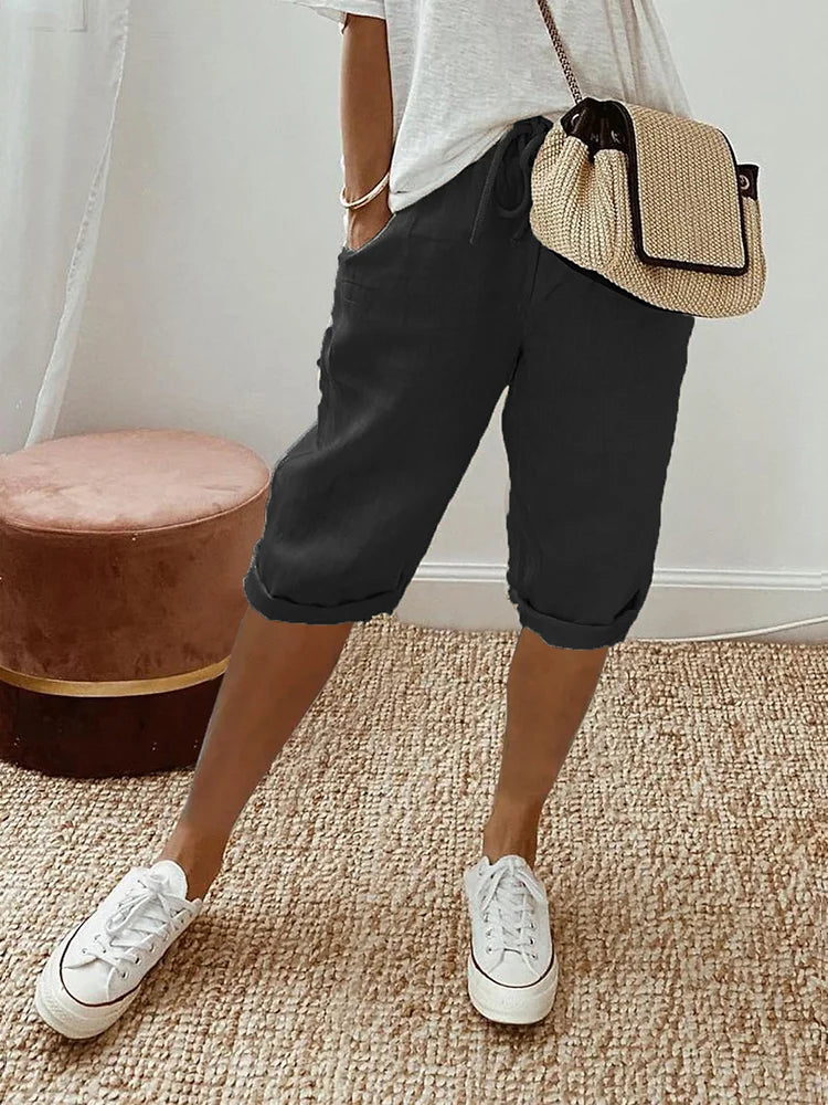 Black comfort shorts matched with a white top and sneakers, showcased in a comfortable indoor room with woven rug and stool.